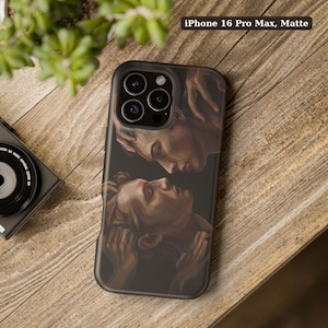 May include: A matte iPhone 16 Pro Max phone case featuring a dark, painterly illustration of two faces positioned close together in a profile view. The artwork displays warm skin tones against a dark background, with visible brushstroke details.