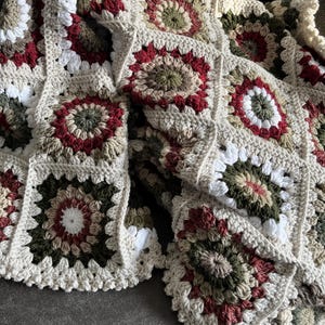 May include: A crocheted throw blanket with a granny square pattern in shades of red, green, white, and brown.