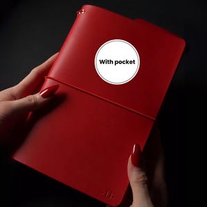 May include: A red leather notebook with an elastic closure. The notebook has a pocket and the text "With pocket" is printed on a white circle. The notebook is held by a person.