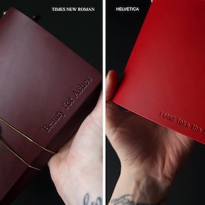 May include: Two leather journals, one burgundy and one red, are displayed. The burgundy journal has the text "Beauty for Ashes" embossed on the cover. The red journal has the text "I shall take the heart" embossed on the cover.