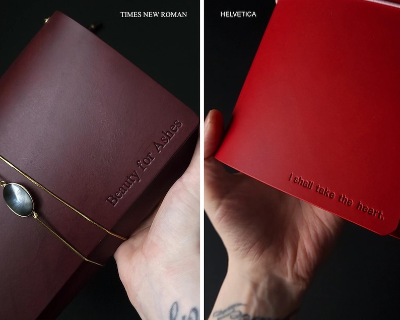 May include: Two leather journals, one burgundy and one red, are displayed. The burgundy journal has the text "Beauty for Ashes" embossed on the cover. The red journal has the text "I shall take the heart" embossed on the cover.