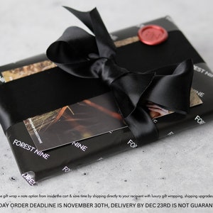 May include: A black gift box with a black satin ribbon and a red wax seal. The box is wrapped in paper with the words "Forest Nine" printed on it.