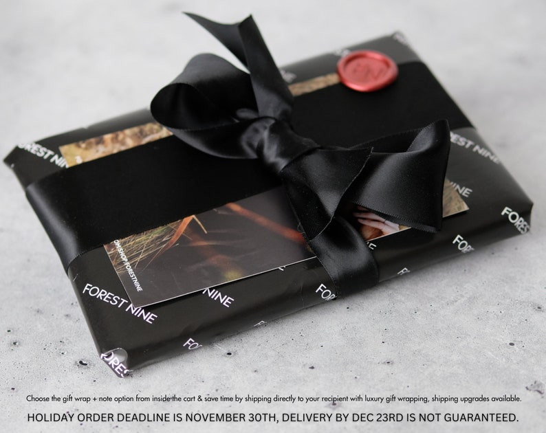 May include: A black gift box with a black satin ribbon and a red wax seal. The box is wrapped in paper with the words "Forest Nine" printed on it.