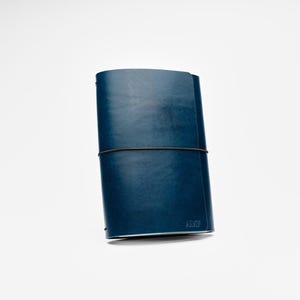 May include: A navy blue leather journal with a black elastic closure. The journal is closed and has a minimalist design. The bottom right corner has the embossed text "AM".