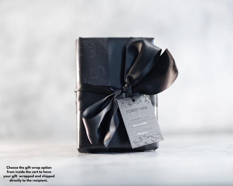 Puede incluir: Una caja de regalo negra con una cinta y un lazo negros. La caja tiene un dise&ntilde;o estampado en blanco y negro. Una etiqueta de regalo con el texto "FOREST NINE" est&aacute; unida a la cinta.