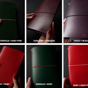 May include: A collection of leather journals in various colors, each secured with an elastic band. Colors include emerald with baby pink, oxblood, violet with black, ruby, and emerald with ruby. Some journals have text.
