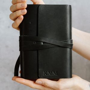 May include: A black leather journal with a strap closure and the initials "KMM" embossed on the front.