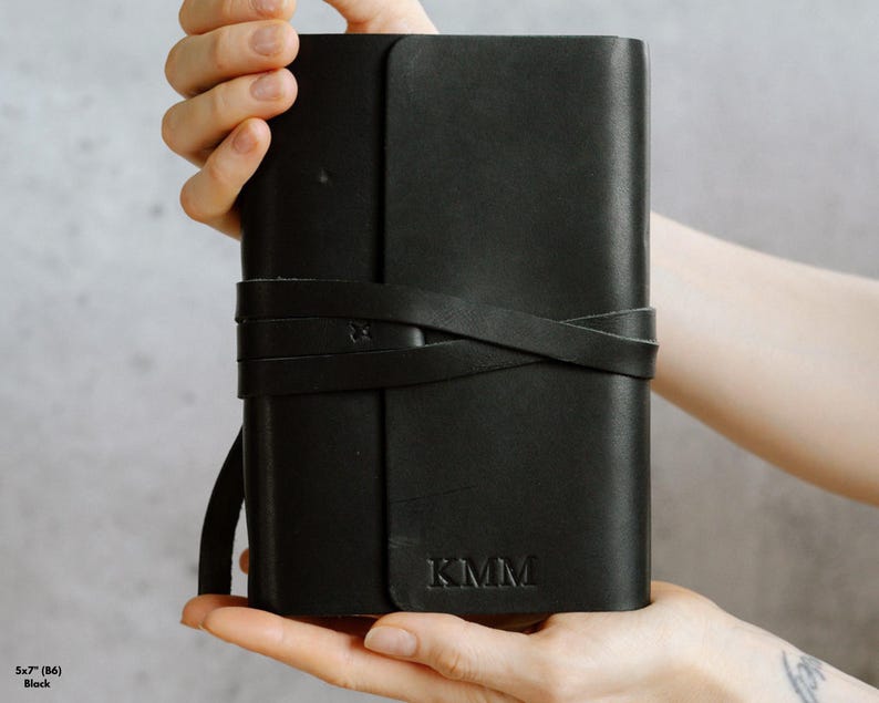 May include: A black leather journal with a strap closure and the initials "KMM" embossed on the front.