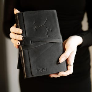 May include: A black leather-bound journal with a constellation design and the initials "PWM" embossed on the cover.