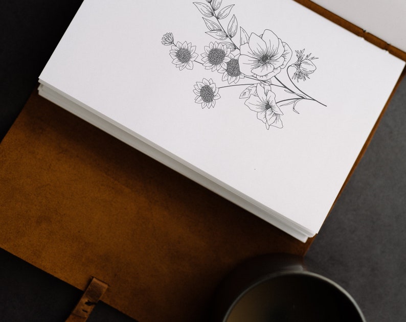 May include: A brown leather journal with a white page open to reveal a black and white line drawing of a bouquet of flowers.