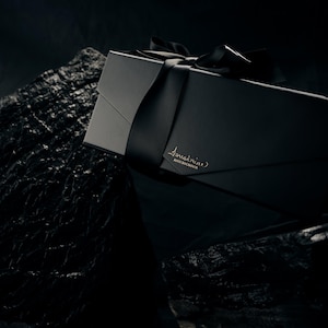 May include: A rectangular black gift box with a matte finish, tied with a matching black satin ribbon. The box features the gold-embossed text 'forestnine' and 'MADE IN CANADA' on the front flap, resting against a dark, textured rock surface.