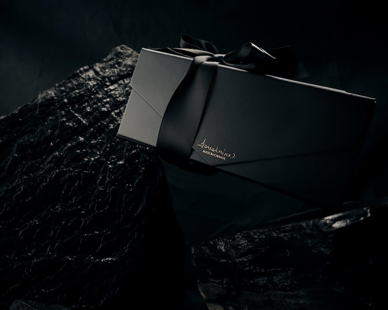 May include: A rectangular black gift box with a matte finish, tied with a matching black satin ribbon. The box features the gold-embossed text 'forestnine' and 'MADE IN CANADA' on the front flap, resting against a dark, textured rock surface.