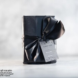 May include: A black gift box with a black ribbon and bow. The box has a black and white patterned design. A gift tag with the text "FOREST NINE" is attached to the ribbon.