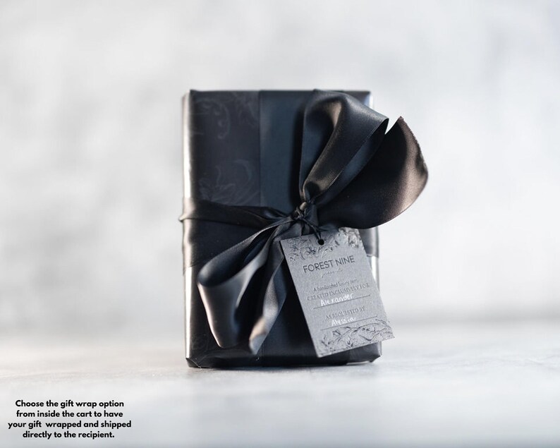 May include: A black gift box with a black ribbon and bow. The box has a black and white patterned design. A gift tag with the text "FOREST NINE" is attached to the ribbon.