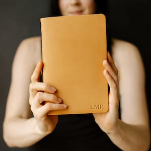 May include: A person holding a tan leather journal with the initials "LMR" embossed on the front.