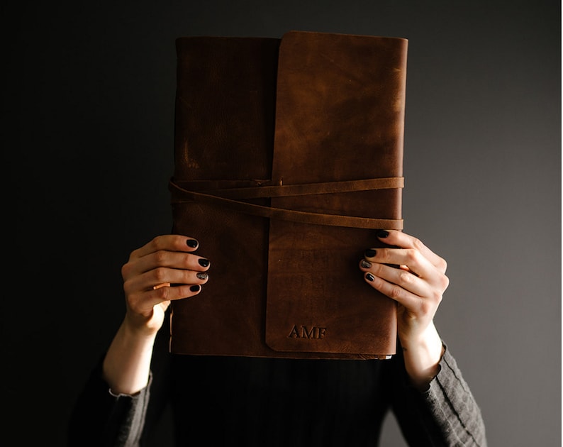 May include: A brown leather journal with a strap closure and the initials "AMP" embossed on the front.