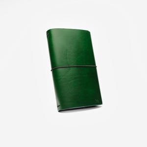 May include: A green leather journal with a black elastic band closure. The journal is rectangular and appears to be made of high-quality leather. The cover is a deep, rich green color.