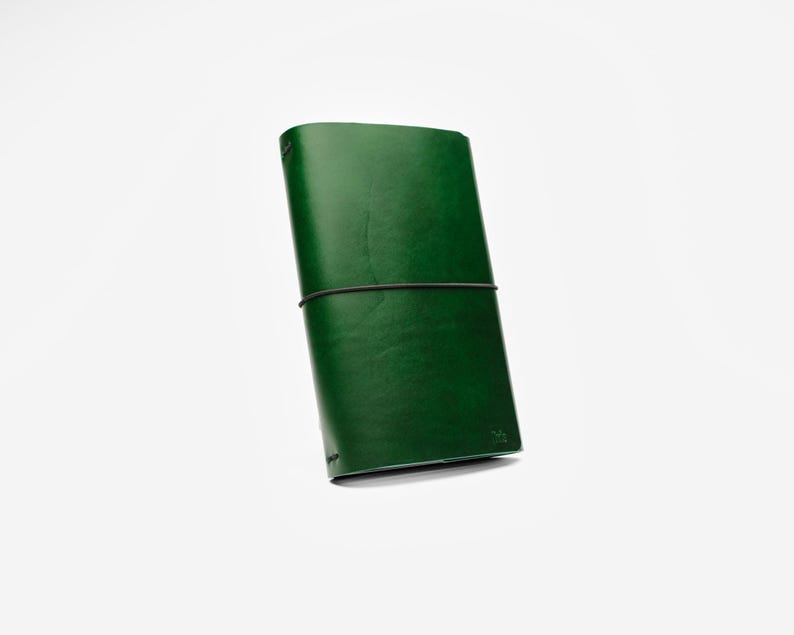 May include: A green leather journal with a black elastic band closure. The journal is rectangular and appears to be made of high-quality leather. The cover is a deep, rich green color.