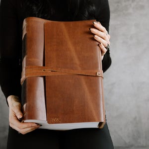 Peut inclure: Un journal relié en cuir marron avec une fermeture à sangle et les initiales "J&J" gravées sur la couverture.