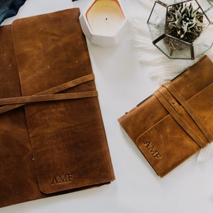 May include: Two brown leather journals with the initials "AMF" embossed on the front. The journals are closed and have leather straps.