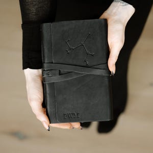 May include: A black leather journal with a constellation design and the initials "PWM" embossed on the cover.