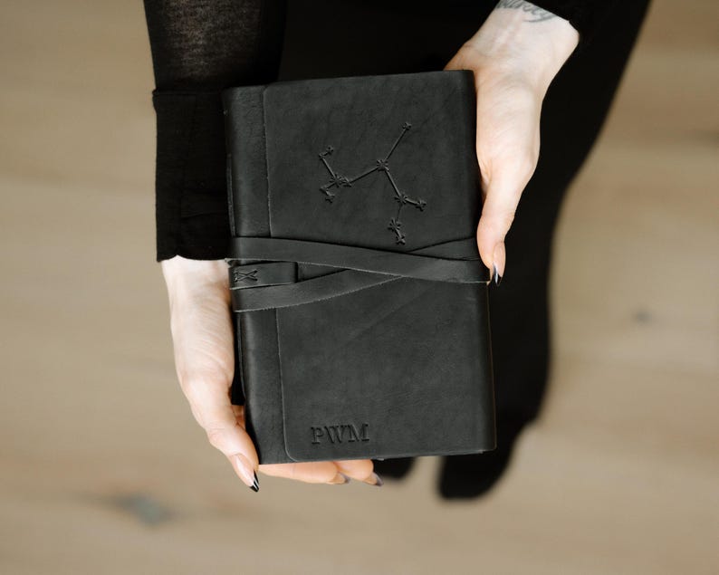 May include: A black leather journal with a constellation design and the initials "PWM" embossed on the cover.
