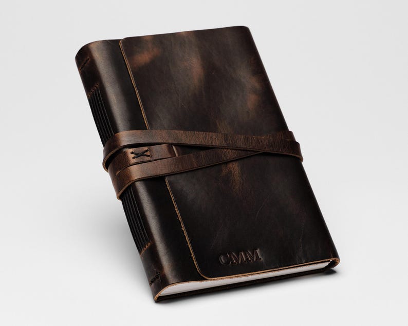 May include: A brown leather journal with a distressed finish and a leather strap closure. The journal has the initials "CMM" embossed on the front cover.
