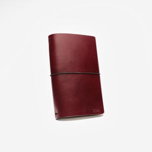 May include: A burgundy leather journal with a black elastic closure. The journal is rectangular and has rounded corners. The word "Vibe" is embossed on the lower right corner. The journal is closed and appears to be new.