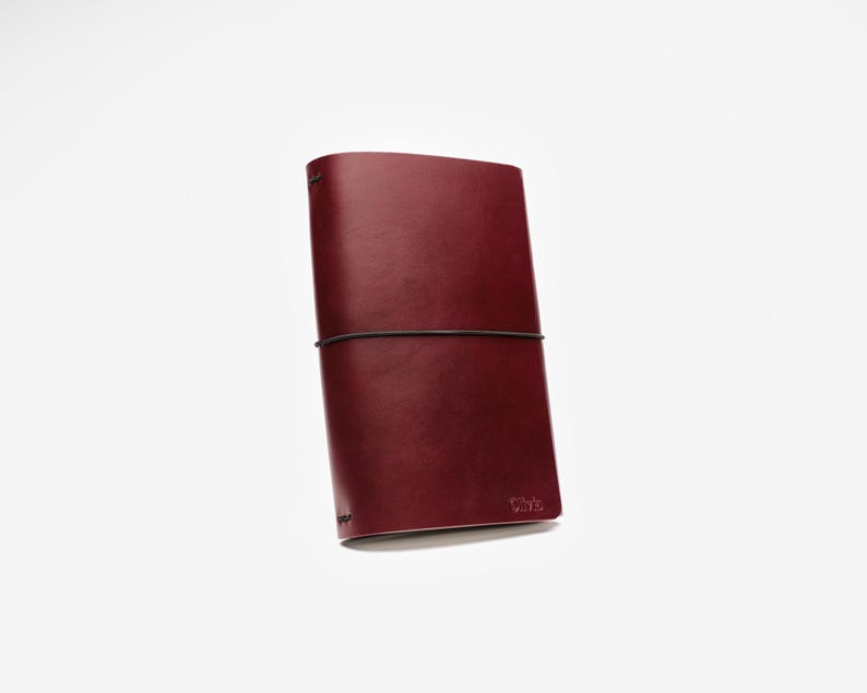 May include: A burgundy leather journal with a black elastic closure. The journal is rectangular and has rounded corners. The word "Vibe" is embossed on the lower right corner. The journal is closed and appears to be new.
