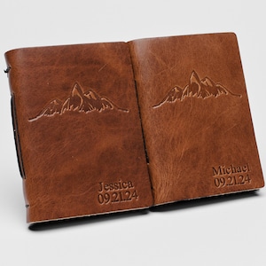 May include: Two brown leather journals with mountain range designs and personalized names and dates. The left journal says "Jessica 09.21.24" and the right journal says "Michael 09.21.24".