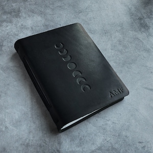 May include: Black leather journal featuring a moon phase design and the initials "AMF" embossed on the cover.