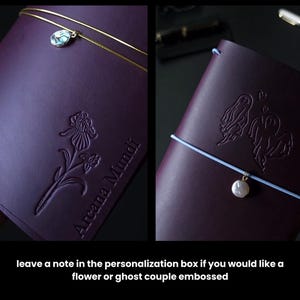 May include: Two dark purple leather journals with embossed designs. One features a flower, the other a ghost couple. Each has a charm and elastic closure. The text "Arcana Mundi" is embossed on one. The image also includes the text: "leave a note in the personalization box if you would like a flower or ghost couple embossed."