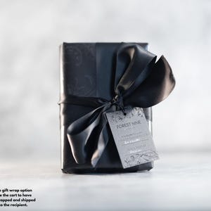 Pode incluir: Uma caixa de presente preta com uma fita e um la&ccedil;o pretos. A caixa tem um design estampado em preto e branco. Uma etiqueta de presente com o texto "FOREST NINE" est&aacute; presa &agrave; fita.
