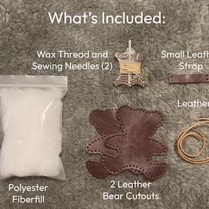 May include: A craft kit containing a clear plastic bag of white polyester fibre-fill, two dark brown leather bear cutouts, a small dark brown leather strap, a tan leather string, and a spool of wax thread with two sewing needles, labelled What's Included.