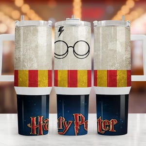 Könnte beinhalten: Ein Edelstahlbecher mit Henkel und Deckel, verziert mit einem Blitzsymbol, einer runden Brille, roten und gelben vertikalen Streifen sowie dem Harry-Potter-Logo in roter und goldener Schrift auf einem dunkelblauen, sternenklaren Hintergrund.