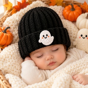 May include: A black ribbed knit beanie featuring a small white crocheted ghost appliqué with black eyes and a smiling mouth. The ghost has tiny orange cheeks. The beanie is made of yarn and has a thick folded brim, providing a textured appearance.