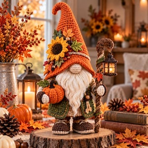 May include: A crocheted gnome figurine wearing a tall orange hat decorated with a sunflower and autumn leaves. The gnome has a long white beard, a green jacket, and brown boots. It holds a small orange pumpkin and a staff with a hanging lantern.