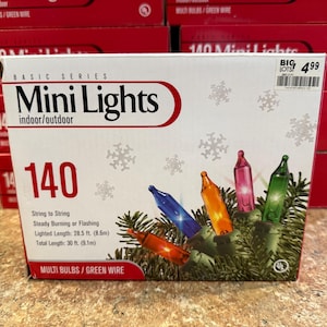 Könnte beinhalten: Ein weißer Karton mit 140 bunten Mini-Lichtern an einem grünen Kabel. Die Verpackung zeigt Schneeflocken-Grafiken sowie den Text 'Basic Series Mini Lights', '140', 'String to String', 'Steady Burning or Flashing' und 'Lighted Length: 8.6m'.