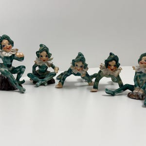 May include: A set of five ceramic elf figurines, each featuring a glossy teal and white mottled glaze. The elves wear pointed hats and ruffled collars, with painted facial features and expressions, posed in various seated and crawling positions.