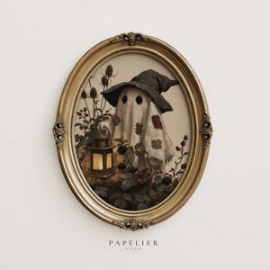 May include: An oval gold ornate frame containing an illustration of a ghost wearing a dark pointed hat and patches, holding a glowing lantern amidst thorny plants with berries. The text PAPELIER STUDIO is printed below the frame.