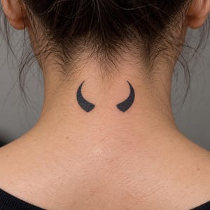 May include: A small, solid black tattoo design located on the back of the neck. The tattoo consists of two symmetrical, curved horn shapes pointing upward and inward toward each other, rendered in a minimalist, bold black ink style.