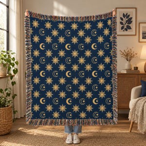 May include: A rectangular woven throw blanket featuring a repeating pattern of yellow suns and crescent moons with stars on a dark blue background. The blanket has a decorative multi-colored fringed edge along all four sides.