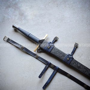 May include: A dark blue leather-wrapped sword hilt with a metallic pommel and crossguard, paired with a matching dark blue leather scabbard featuring intricate embossed scrollwork, brass-toned accents, and a long adjustable leather belt strap.