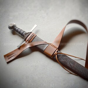 May include: A sword with a dark grey hilt and a spherical pommel featuring a cross emblem. The blade is encased in a dark brown scabbard with a textured geometric pattern, secured by a light brown leather belt with metal hardware and lacing.