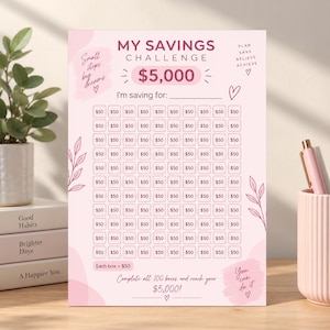 Puede incluir: Una hoja de seguimiento de ahorros rosa con el texto My Savings Challenge $5,000. Incluye 100 casillas individuales marcadas con $50, una línea para I'm saving for, e ilustraciones decorativas de hojas, corazones y frases motivadoras.