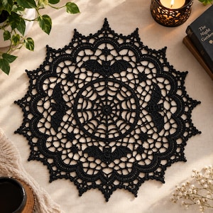 Peut inclure: Un napperon circulaire en crochet noir présentant un motif central de toile d'araignée entouré d'une bordure en dentelle délicate avec des motifs de chauves-souris intégrés. Le travail d'aiguille crée un design symétrique et détaillé.