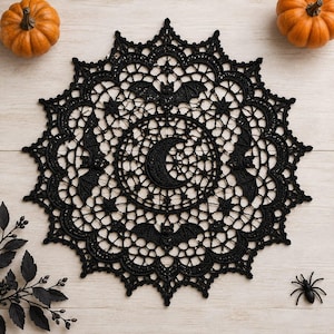 May include: A circular black crochet doily featuring a central crescent moon motif surrounded by a detailed web-like pattern with integrated bat silhouettes and small star shapes. The intricate lace design has a scalloped edge and a dark thread texture.