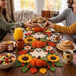 Peut inclure: Un chemin de table en crochet orné de citrouilles orange, de fantômes blancs, de tournesols jaunes et de feuilles d'automne rouges et orange. Il est posé sur une table en bois avec des tasses, un pichet de jus, des fruits et des pancakes.