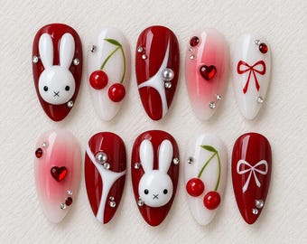 May include: A set of ten almond-shaped press-on nails featuring a red and white color palette. Designs include 3D white rabbit figures, red cherries, red and white bows, red heart-shaped rhinestones, and small clear crystals on glossy surfaces.