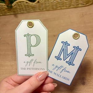May include: Two rectangular paper gift tags with rounded top corners and gold metal eyelets. One tag features a green letter P with the text a gift from THE PATTERSONS. The other tag features a blue letter M with the text a gift from THE MALLARDS.